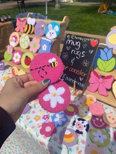 a person is holding up some crocheted items at an outdoor market table with flowers and bugs on them