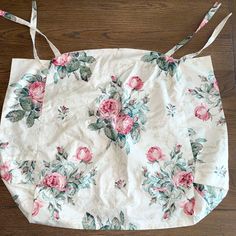 a white floral bag with pink roses on it sitting on a wooden floor next to a pair of scissors