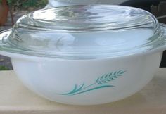 a glass bowl sitting on top of a wooden table next to a white plate with a green leaf design