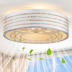 a white ceiling light with green leaves flying around it in the middle of a room