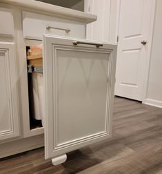 an open cabinet door in the middle of a kitchen with wood floors and white cabinets