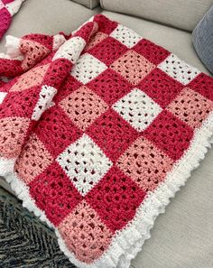 a red and white crocheted blanket sitting on top of a couch next to a pillow