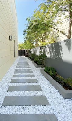 an outdoor walkway with stepping stones leading to the side of a house, surrounded by trees and shrubs