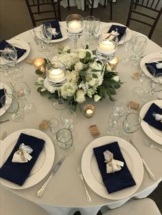 a table set with white and blue place settings, silverware, candles and napkins