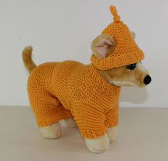 a stuffed dog wearing an orange knitted sweater and beanie hat, standing on a white surface