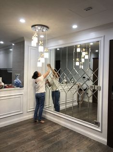 a woman standing in front of a mirror holding onto the side of a wall with lights on it