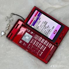 a red electronic device sitting on top of a white blanket next to a key chain