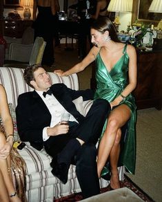 a man in a tuxedo sitting on a couch next to a woman in a green dress