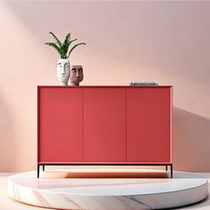 a red cabinet sitting on top of a white table next to a potted plant