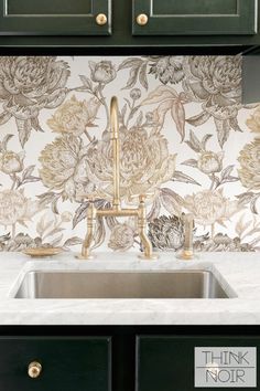 a kitchen sink under a faucet in front of a floral wallpaper