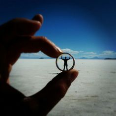 a hand holding a ring with a man standing in the middle of an empty field