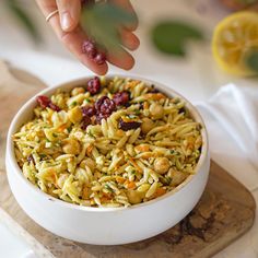 someone is sprinkling cranberries on top of a pasta salad in a white bowl