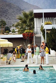 people are in the swimming pool with umbrellas and chairs around them while others watch