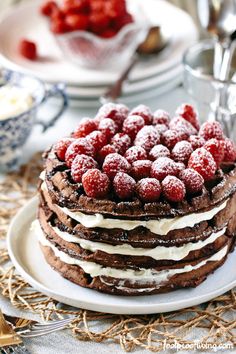 a chocolate cake topped with raspberries on top of a white plate next to silverware