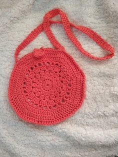 A red crochet round bag laid flat on a bed.