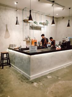 two people sitting at a bar with drinks on the counter and lights hanging above them