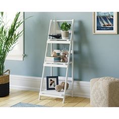 a white ladder shelf with pictures and plants on it next to a blue wall in a living room