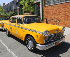 two yellow taxi cabs parked in front of a brick building