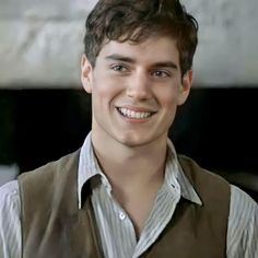 a young man smiling at the camera with his hair pulled back and wearing a vest