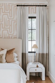 a white bed sitting under a window next to a lamp on top of a wooden floor