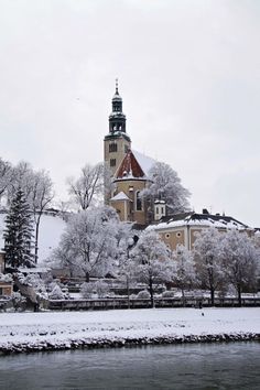 a large building with a clock tower in the middle of it's center surrounded by snow covered trees