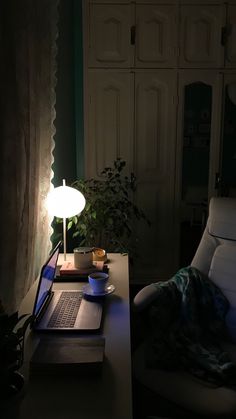 a laptop computer sitting on top of a wooden desk next to a lamp in a dark room