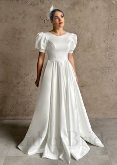 a woman in a white wedding dress standing against a wall with her hands on her hips