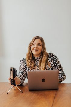 a woman sitting at a table with an apple laptop in front of her, holding a camera