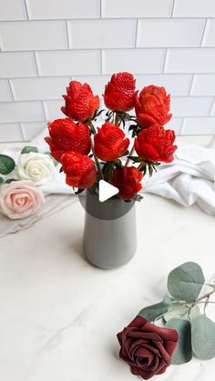 a vase filled with red and white flowers on top of a marble table next to roses