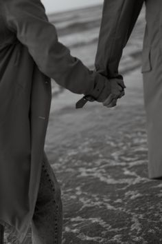 two people holding hands while walking on the beach