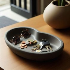 there is a tray with keys and sunglasses on the table next to a potted plant