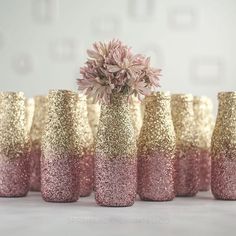 pink and gold glitter vases lined up on a table with flowers in the middle