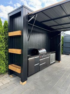 an outdoor kitchen is built into the side of a building with black siding and wood shelves