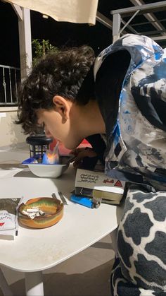 a young man is looking at an object on a table with other items around him