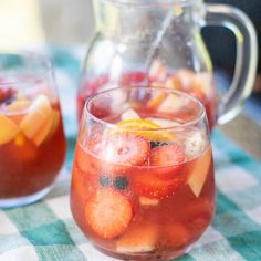 a pitcher filled with liquid next to two glasses full of fruity drinks on a checkered table cloth