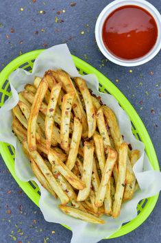 some french fries on a green plate next to a cup of ketchup and sauce