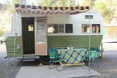 an old camper trailer with a table and chairs in front of it on gravel