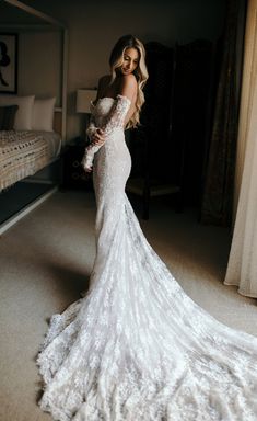 a woman in a wedding dress is standing near a bed and looking at the camera