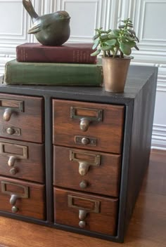 a bird figurine sitting on top of an old filing cabinet with two books