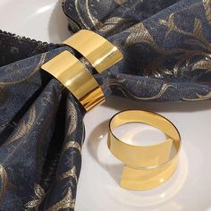 two gold rings sitting on top of a white plate next to a blue scarf and napkin