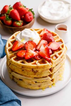 a stack of waffles topped with strawberries and whipped cream next to a bowl of fruit