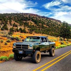 a truck is driving down the road in front of some grass and trees with mountains in the background