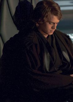 the young man is sitting down looking at his cell phone while wearing a black robe