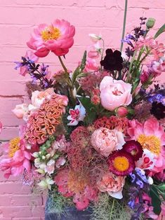 a vase filled with lots of colorful flowers on top of a table next to a brick wall