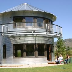 two people sitting on a bench in front of a round metal building with balconies