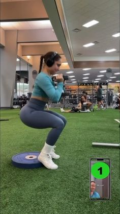 a woman squats on a blue mat while holding a cell phone in front of her