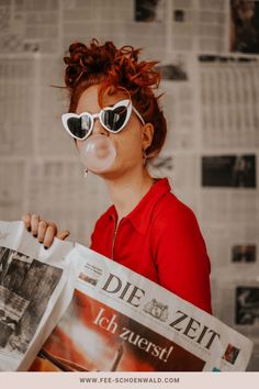 a woman with red hair wearing sunglasses and reading a newspaper in front of her face