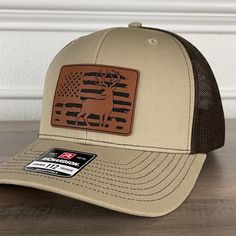 Deer Hunting American Flag Patriotic Leather Patch Hat Khaki/Brown. Specifications: 🧢 Richardson original 112 trucker; adjustable for the perfect fit 🎩 60/40 cotton/polyester blend for comfort 📏 One size fits most 🏷️ Expertly laser engraved leatherette patch design 📦 Ships in 2 to 3 business days from our Orlando Studio Care Instructions: 🚫 Do not wash; spot clean only Please Note: 🌈 Colors may vary from photos based on your viewing screen. Brown Flat Brim Country Baseball Cap, Brown Flat Brim Country Style Baseball Cap, Country Style Brown Baseball Cap With Flat Brim, Country Style Brown Flat Brim Baseball Cap, Brown Country Style Baseball Cap With Curved Brim, Brown Country Style Snapback Hat With Flat Bill, Country Style Brown Snapback Hat, Country Style Brown Snapback Hat With Flat Bill, Brown Country Style Trucker Hat With Flat Bill