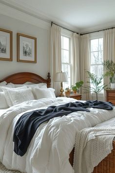 a bed with white comforter and pillows in a bedroom next to two large windows