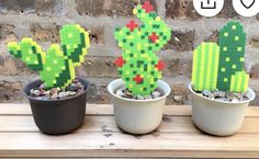 three potted plants with pixelated cactuses in them sitting on a wooden table